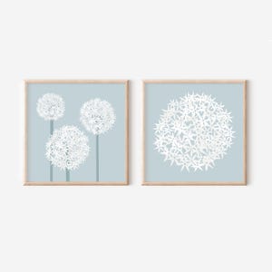 May include: Two framed prints with a blue background and white flower illustrations. The print on the left features three white flowers with stems. The print on the right features a single white flower.