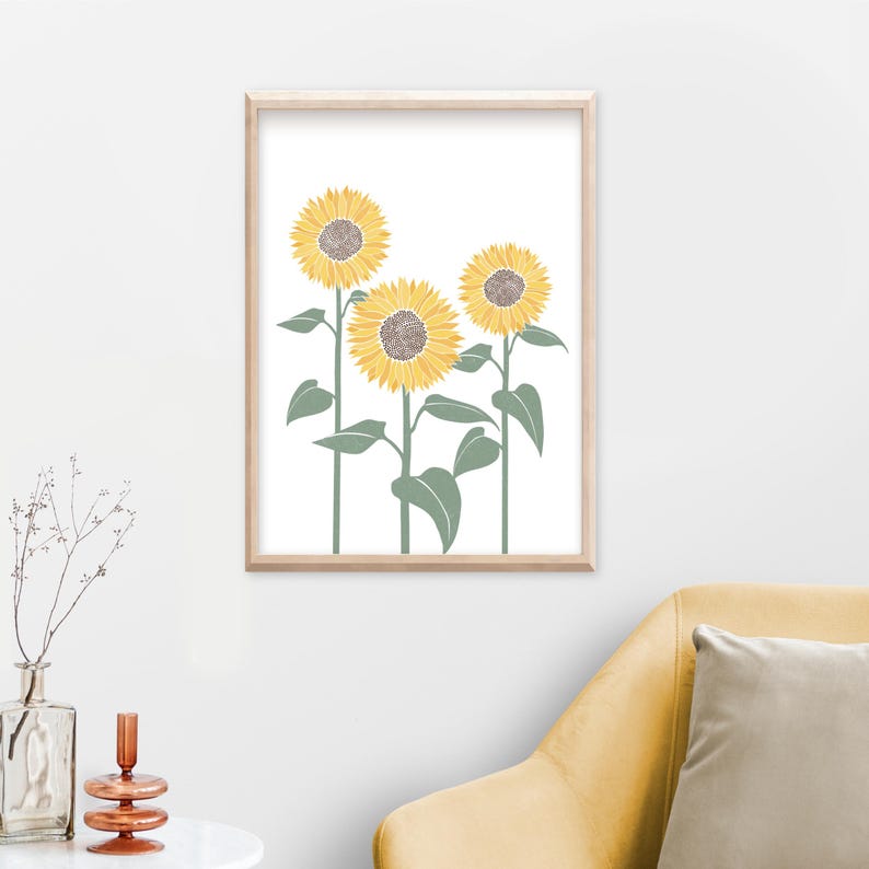 K&ouml;nnte beinhalten: Ein gerahmter Wandkunstdruck mit drei Sonnenblumen mit gelben Bl&uuml;tenbl&auml;ttern und braunen Mitten auf wei&szlig;em Hintergrund. Die Sonnenblumen haben lange gr&uuml;ne St&auml;ngel und gr&uuml;ne Bl&auml;tter, alles in einem hellen Holzrahmen eingefasst.