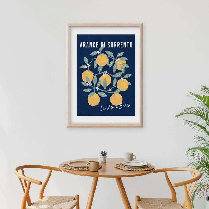 May include: A framed wall art print featuring a dark blue background with a central illustration of yellow oranges on green leafy branches. The text ARANCE DI SORRENTO is printed in white at the top, and La Vita &egrave; Bella is in white script below.