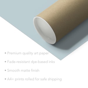 May include: A brown cardboard tube with a white edge, rolled up for safe shipping. The tube is on a light blue background with text describing the product's features: premium quality art paper, fade-resistant dye-based inks, smooth matte finish, and A4+ prints rolled for safe shipping.