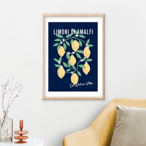 May include: A framed wall art print featuring a dark blue background with yellow lemons, green leaves, and white blossoms. The text LIMONI DI AMALFI is printed in white at the top, and the text La Dolce Vita is printed in white at the bottom.