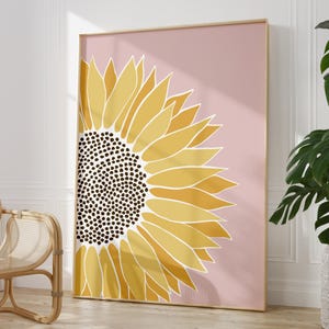 May include: A large, stylized sunflower with a yellow and brown center on a pink background. The sunflower is in a gold frame.