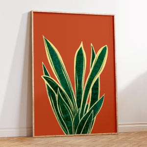 May include: A framed print of a stylised illustration of a green and yellow snake plant on a burnt orange background.