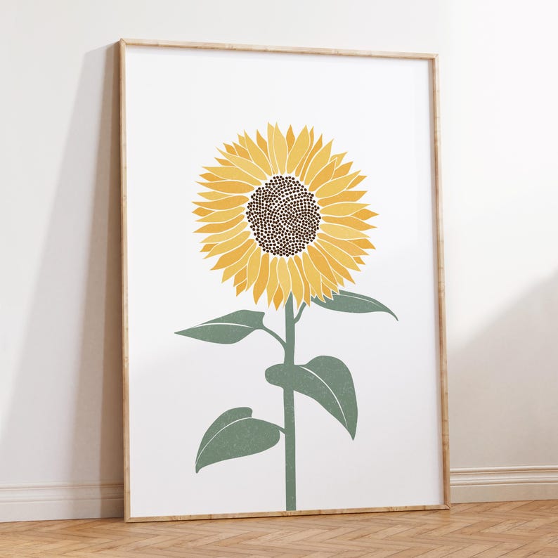 K&ouml;nnte beinhalten: Ein gerahmter Wandkunstdruck, der eine einzelne Sonnenblume mit leuchtend gelben Bl&uuml;tenbl&auml;ttern und einer dunkelbraunen Mitte vor einem schlichten wei&szlig;en Hintergrund zeigt. Die Blume hat einen gr&uuml;nen Stiel und drei gr&uuml;ne Bl&auml;tter.