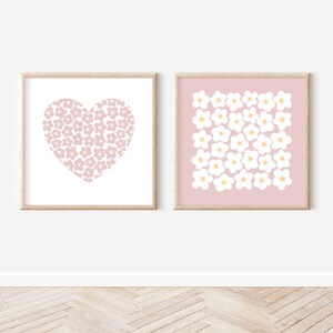 May include: Two framed prints with a pink background and white floral designs. One print features a heart shape filled with flowers, while the other print has a grid of flowers.