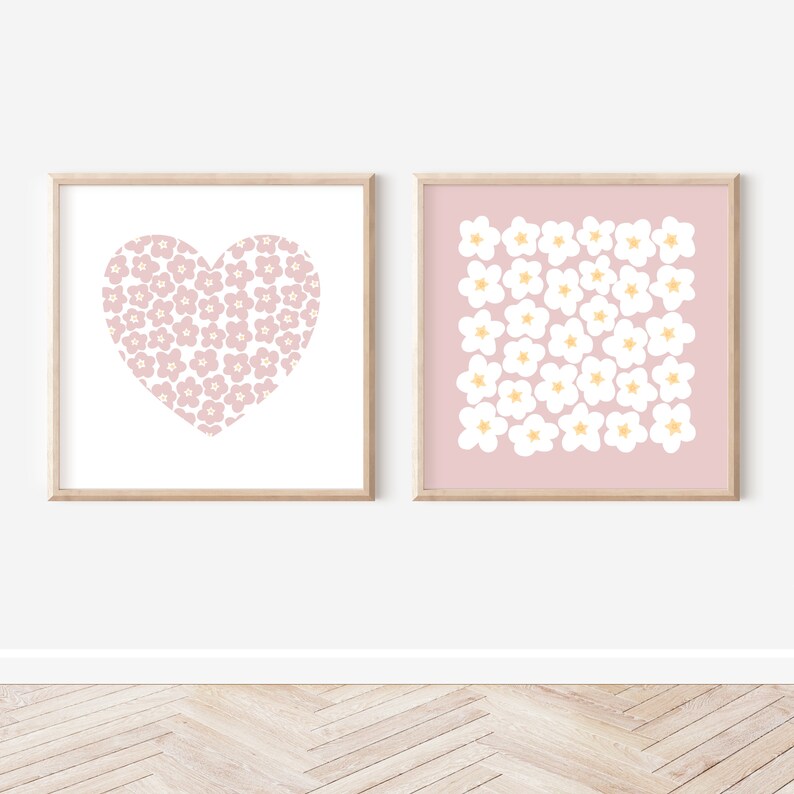 May include: Two framed prints with a pink background and white floral designs. One print features a heart shape filled with flowers, while the other print has a grid of flowers.