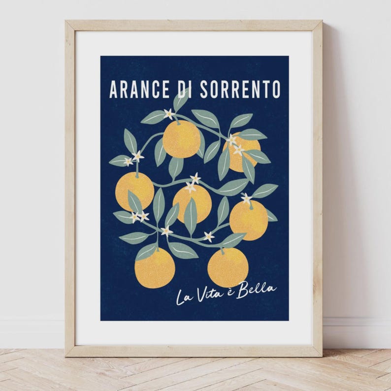 May include: A framed wall art print featuring a dark blue background with yellow oranges, green leaves, and white blossoms. The text ARANCE DI SORRENTO is printed in white at the top, and the text La Vita &egrave; Bella is printed in white at the bottom.