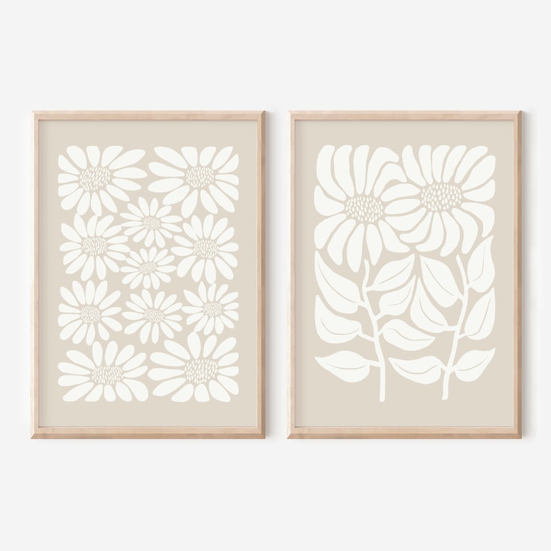 May include: Two beige framed prints with white floral designs. The print on the left features a repeating pattern of stylized white flowers. The print on the right features a cluster of stylized white flowers with leaves.
