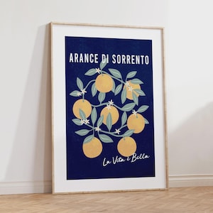 May include: A framed vertical art print featuring a deep navy blue background with a central illustration of orange branches bearing yellow oranges and small white blossoms. The text ARANCE DI SORRENTO and La Vita &egrave; Bella is printed in white.