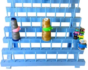 May include: A blue plastic thread rack with multiple rows of pegs for holding spools of thread. The rack is angled and has a set of extra pegs included.