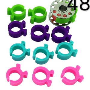 May include: A set of 48 colorful plastic thread bobbin holders. The holders are in four colors: green, purple, turquoise, and pink. The set includes a small spool of thread.