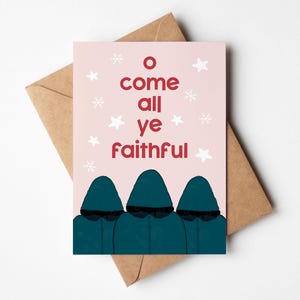 Puede incluir: Una tarjeta de Navidad con el texto "O come all ye faithful" en rojo sobre un fondo rosa, con copos de nieve y estrellas blancas. La tarjeta presenta tres figuras con túnicas color teal. La tarjeta está sobre un sobre marrón.