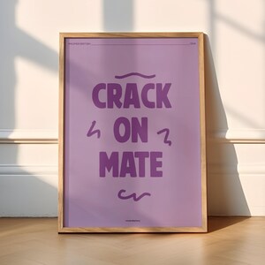 Op de afbeelding: Een ingelijst print met een paarse achtergrond en de tekst "CRACK ON MATE" in een vet, paars lettertype.