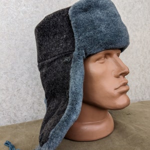 May include: A grey and black winter hat with a fur trim and a long, blue cord. The hat is made of wool and has a button on the side.