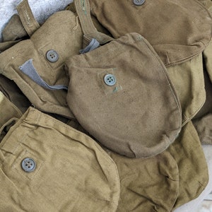 May include: A group of five olive green canvas pouches with button closures. The pouches are stacked on top of each other.