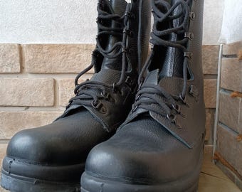 Op de afbeelding: Een paar zwarte leren combat boots met hoge schachten en dikke zolen. De laarzen hebben meerdere veterogen en zijn ontworpen voor ruig gebruik. De laarzen worden gepresenteerd op een neutraal gekleurd oppervlak.