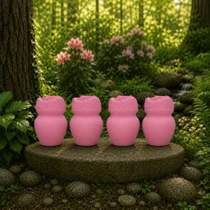 May include: Four pink, flower-shaped containers are displayed on a stone surface in a garden. The containers have a rounded body and a scalloped top, resembling a blooming flower. The background features lush greenery and a small waterfall.