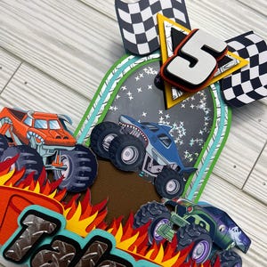 May include: A colorful birthday card featuring monster trucks, flames, and checkered flags. The card includes the name "Talon" and the number "5". The monster trucks are orange, blue, and green, with large tires.