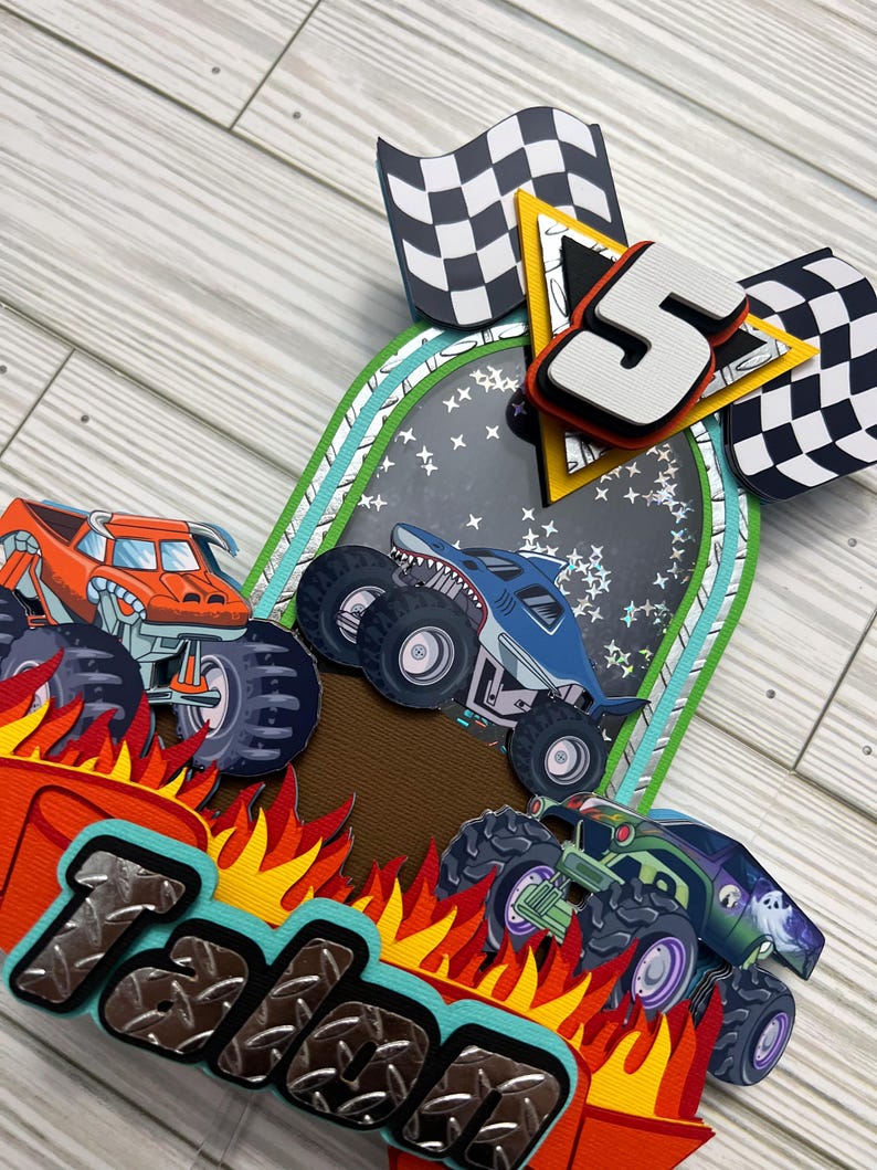May include: A colorful birthday card featuring monster trucks, flames, and checkered flags. The card includes the name "Talon" and the number "5". The monster trucks are orange, blue, and green, with large tires.