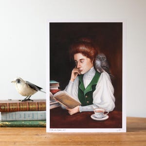 Può includere: Un dipinto di una donna con i capelli rossi che legge un libro con un gufo appollaiato sulla sua spalla. Indossa un gilet verde e una blusa bianca. C'è una tazza di tè e una pila di libri sul tavolo di fronte a lei.