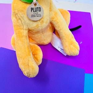 Pu&ograve; includere: Un giocattolo di peluche di Pluto, il cane, con un collare verde e un'etichetta che dice "PLUTO se trovato, per favore restituiscilo a MICKEY MOUSE".