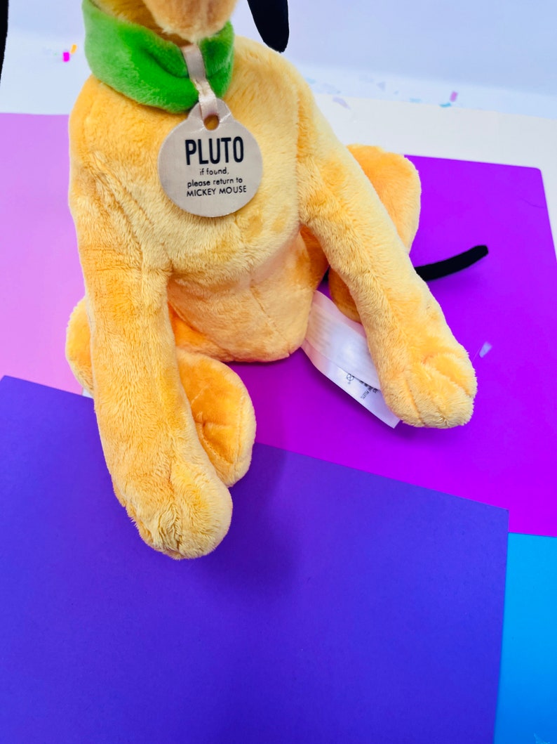 Pu&ograve; includere: Un giocattolo di peluche di Pluto, il cane, con un collare verde e un'etichetta che dice "PLUTO se trovato, per favore restituiscilo a MICKEY MOUSE".