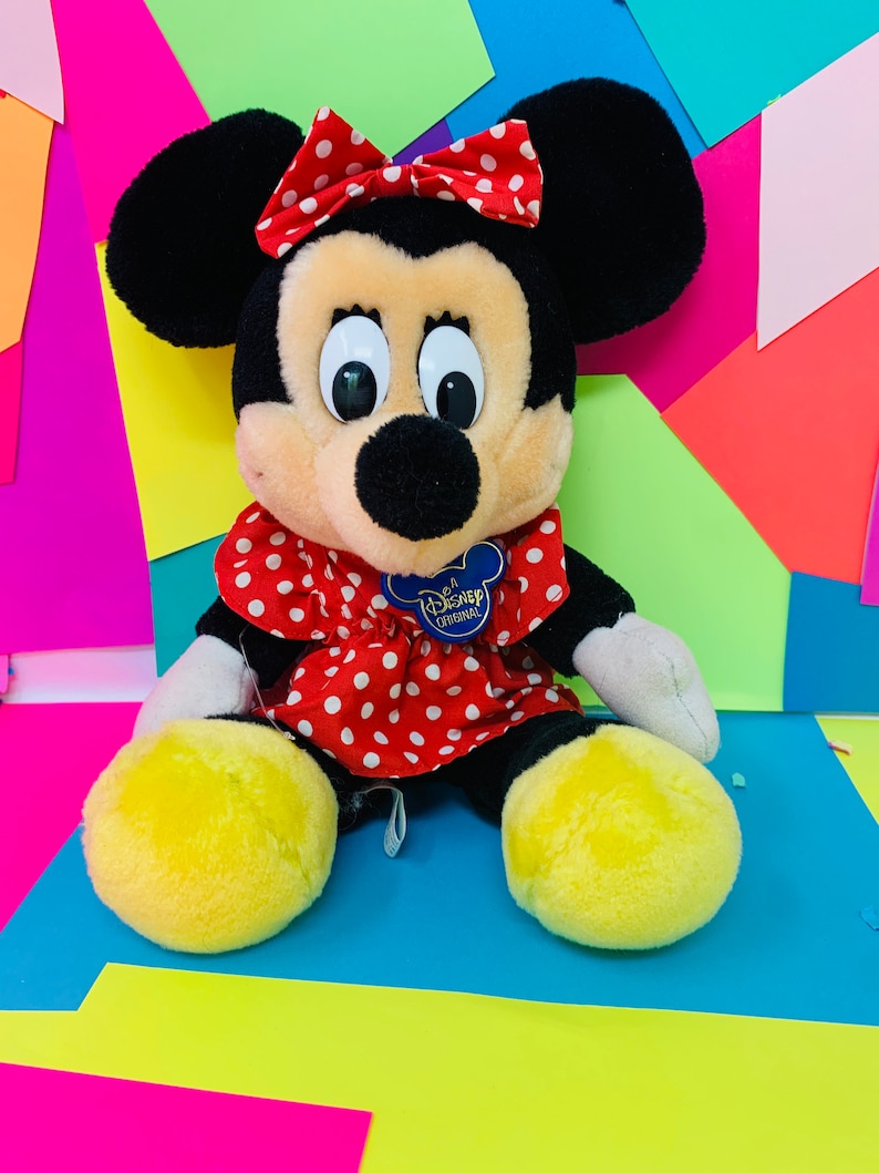 May include: A plush Minnie Mouse toy wearing a red dress with white polka dots and a red bow with white polka dots. The toy has a yellow Disney Original tag on its chest.
