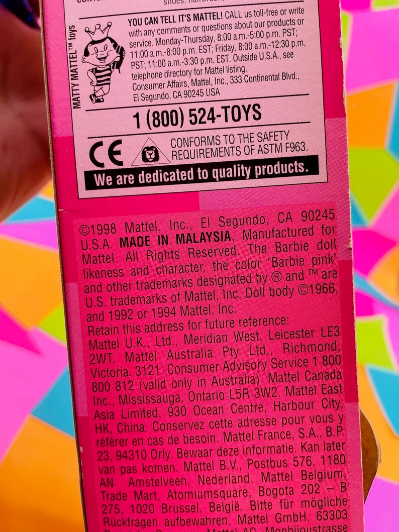 May include: Pink and white Barbie doll packaging with a pink background and a white border. The packaging features a photo of the Barbie doll and the text "YOU CAN TELL IT'S MATTEL!" and "MADE IN MALAYSIA".