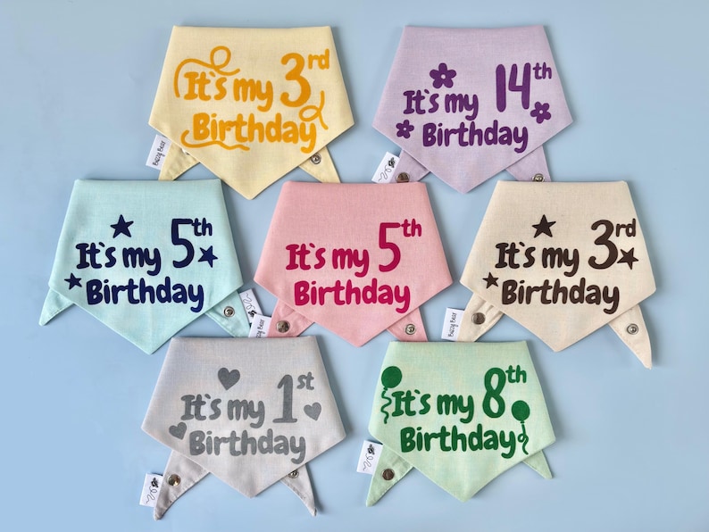 Op de afbeelding: Een verzameling pastelkleurige hondenbandana's met de tekst "It's my [number] Birthday". Elke bandana heeft een andere kleur en bevat de zin in verschillende lettertypen en kleuren. De cijfers vari&euml;ren van 1 tot en met 14.