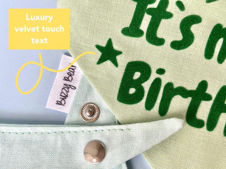 Op de afbeelding: Een lichtgroene hondenbandana met de tekst "It's my Birth" in groen, samen met een groene ster. De bandana heeft een drukknoopsluiting en een label met "Buzzy Bear".