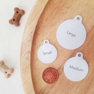May include: Three round dog tags on a wooden surface. The tags are labeled "Small", "Medium", and "Large".