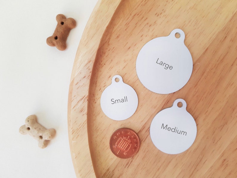 May include: Three round dog tags on a wooden surface. The tags are labeled "Small", "Medium", and "Large".
