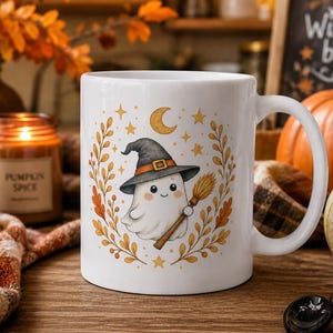 Puede incluir: Taza de cer&aacute;mica blanca con un fantasma de dibujos animados con un sombrero de bruja y una escoba. La taza est&aacute; decorada con estrellas, una luna creciente y hojas de oto&ntilde;o. El fondo incluye calabazas, velas y un letrero que dice "Witches brew".