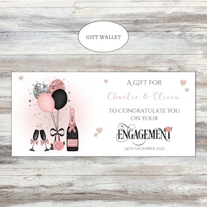 May include: A rectangular gift wallet featuring a champagne bottle, two glasses, and balloons in black, pink, and glittery rose gold. The text reads: A GIFT FOR Charlie & Olivia TO CONGRATULATE YOU ON YOUR ENGAGEMENT 24TH DECEMBER 2023.