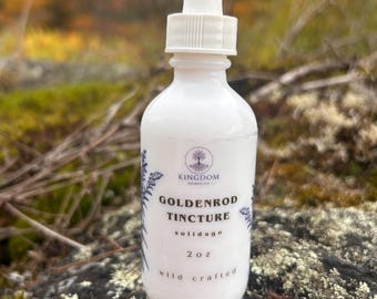 Puede incluir: Un frasco cuentagotas de vidrio blanco con tintura de vara de oro. La etiqueta muestra un logotipo de árbol, el texto Kingdom Remedies, Goldenrod Tincture, solidago, 2 oz y wild crafted. El frasco tiene un tapón blanco.