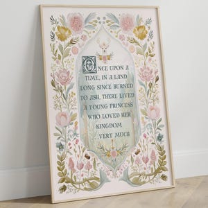 May include: A framed art print with a floral and botanical design. The artwork includes the text: "ONCE UPON A TIME, IN A LAND LONG SINCE BURNED TO ASH, THERE LIVED A YOUNG PRINCESS WHO LOVED HER KINGDOM VERY MUCH". The frame is a light colour.