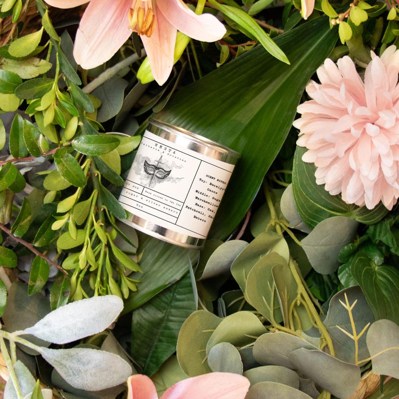 Puede incluir: Una lata de vela plateada con una etiqueta blanca que presenta una ilustraci&oacute;n en blanco y negro de una m&aacute;scara. La etiqueta dice "Home Scent" y enumera las notas de olor:  Salida - Bergamota, Pomelo, Coraz&oacute;n - Jazm&iacute;n, Malvavisco, Fondo - Pachul&iacute;, Cedro, &Aacute;mbar.