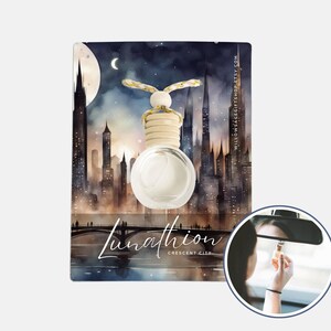 May include: Car air freshener with a clear, round glass bottle and a wooden cap, hanging in front of a cityscape illustration. The illustration features a crescent moon and the text "Lunathion Crescent City". The product is shown in a car's rearview mirror.