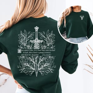 May include: A dark green sweatshirt with a white floral design featuring a sword and the quote "Once upon a time, in a land long since burned to ash, there lived a young princess who loved her kingdom... very much."
