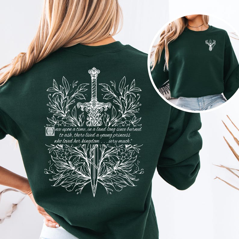 May include: A dark green sweatshirt with a white floral design featuring a sword and the quote "Once upon a time, in a land long since burned to ash, there lived a young princess who loved her kingdom... very much."