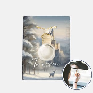 以下が含まれることがあります： 冬の風景を背景に吊るされた、木製のトップと装飾的なコードが付いた透明なガラス製の車用芳香剤。カードには城、木、鹿が描かれています。「Terrasen Erilea」の文字が見えます。