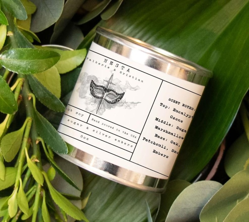 Puede incluir: Una vela en una lata de plata con una etiqueta en blanco y negro que presenta una m&aacute;scara de carnaval y una espada. La etiqueta dice "NESTA Valkerie & Orintin" y enumera las notas de olor: "Top: Eucalipto, Ozono, Middle: Az&uacute;car, Malvavisco, Base: Roble, Pachul&iacute;, Humo, Brasas".