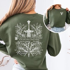 May include: A green sweatshirt with a white design of a sword surrounded by leaves and a quote that reads "once upon a time, in a land long since burned to ash, there lived a young princess who loved her kingdom... very much."