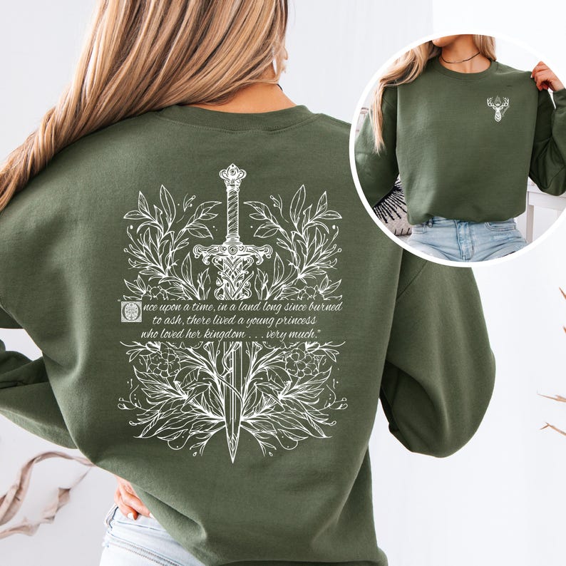 May include: A green sweatshirt with a white design of a sword surrounded by leaves and a quote that reads "once upon a time, in a land long since burned to ash, there lived a young princess who loved her kingdom... very much."