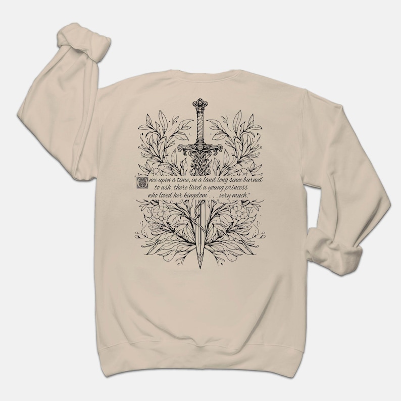 May include: A beige long-sleeve sweatshirt with a black and white illustration of a sword surrounded by floral designs. The text "once upon a time, in a land long since burned to ash, there lived a young princess who loved her kingdom... very much." is printed on the sweatshirt.