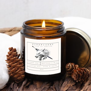 May include: A lit, amber-colored glass jar candle with a silver lid. The label reads "KINGFISHER lord of oakhish" with a wolf illustration. The candle is 4 oz and made with coconut soy. The scent is morning air, pine & smoke.