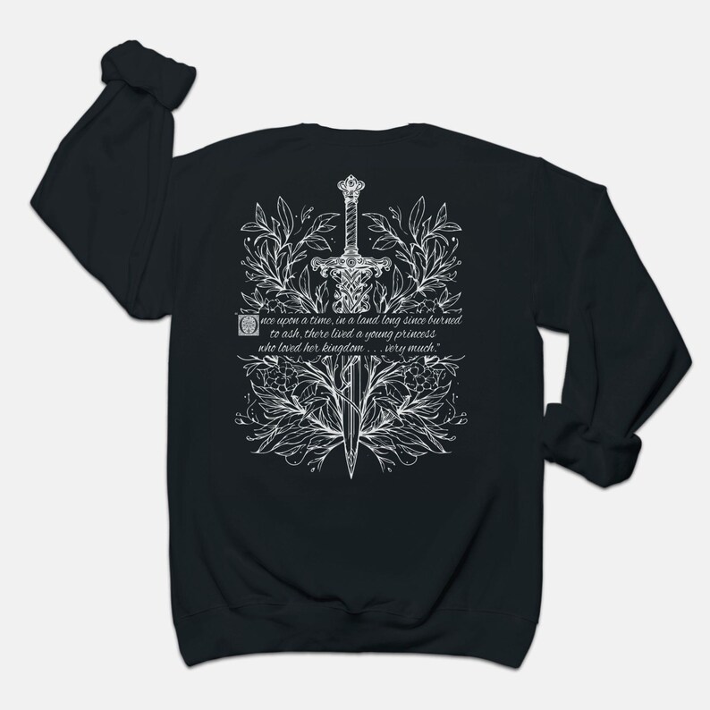 May include: Black long-sleeve sweatshirt with a white graphic design of a sword surrounded by flowers and leaves. The text "once upon a time, in a land long since burned to ash, there lived a young princess who loved her kingdom... very much." is printed on the sweatshirt.