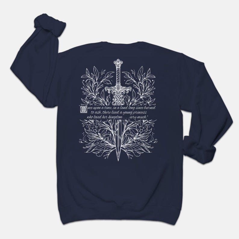 May include: Navy blue long-sleeve sweatshirt with a white design of a sword surrounded by flowers and leaves. The text "once upon a time, in a land long since burned to ash, there lived a young princess who loved her kingdom... very much." is printed on the sweatshirt.