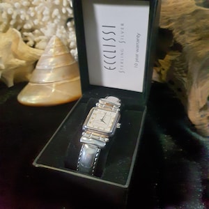 New in Box Ecclissi Sterling Silver Watch. Half Black Leather & 925 Band. New Battery 8/25. Small Dent in Back, not visible. 1980-1990 Era