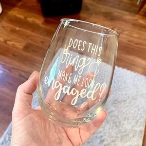 May include: A clear glass wine glass with the text "Does this ring make me look engaged?" printed on it.
